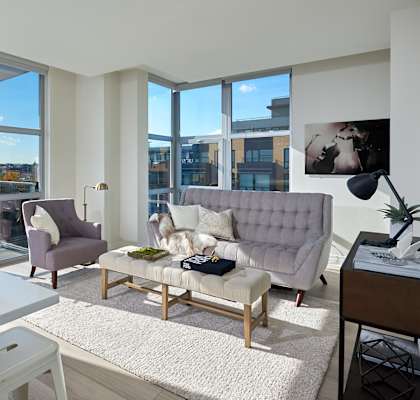 A modern living room with a grey sofa, a white table, and a large window overlooking the city.