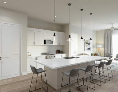 A modern kitchen with a long white island and grey chairs.