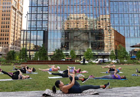 A group of people doing yoga in a park with a large glass building in the background.