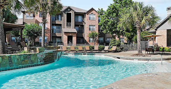 A swimming pool surrounded by palm trees and a building in the background.