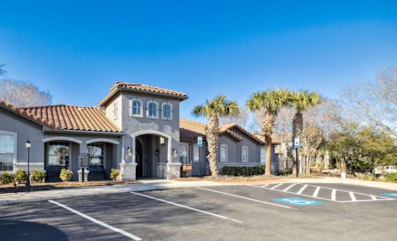 A building with a red tile roof and a parking lot in front.