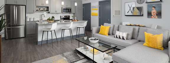 A modern kitchen with a bar and a grey couch with yellow pillows.