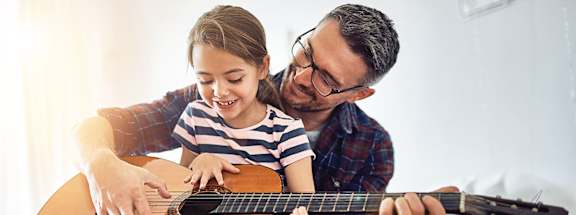 A man is teaching a young girl how to play the guitar.