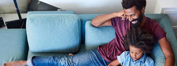 A man and a child are sitting on a blue couch.