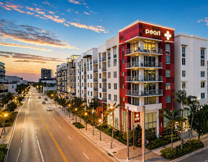 A red and white hotel named Pearl is located on a street with cars parked on the side.