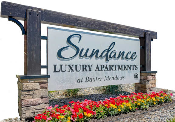 A sign for Sundance Luxury Apartments at Baxter Meadows is displayed in front of flowers.