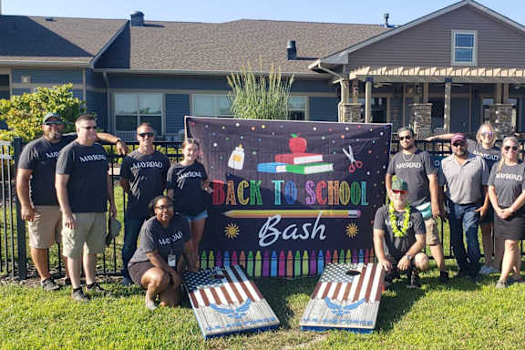 A group of people are posing in front of a sign that says "Back to School Bash".