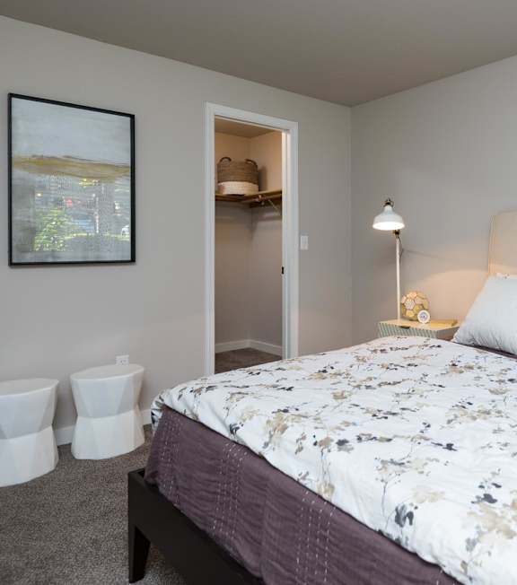 A bedroom with a bed, nightstand, and two stools.