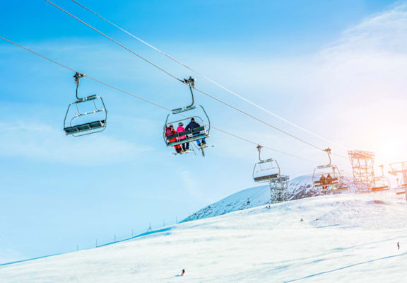A ski lift with two gondolas carrying skiers up a snowy mountain.