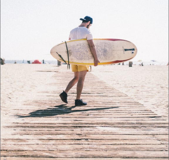 Man Walking Along Beach Holding Surfboard