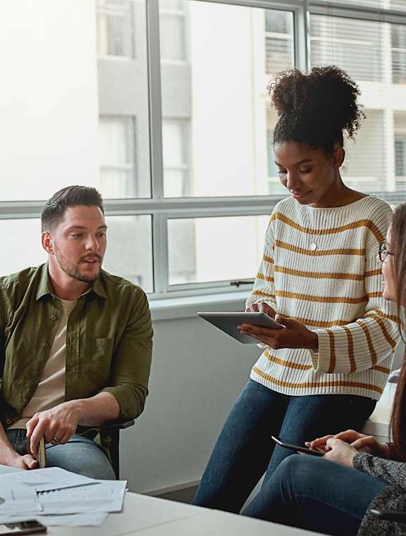 Four people are sitting around a table with papers and a tablet, engaged in a discussion.