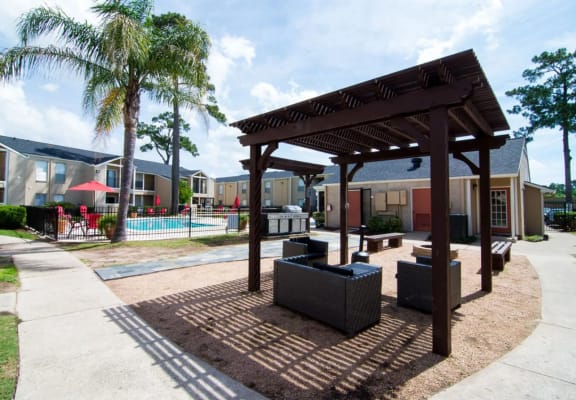 a pergola sits in front of a swimming pool with a pool house in the background