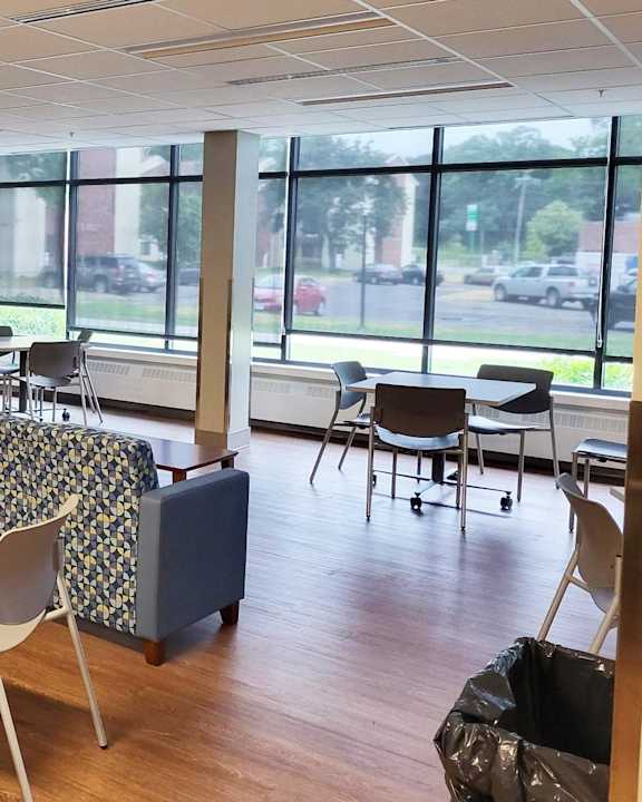A room with tables and chairs and a window overlooking a parking lot.
