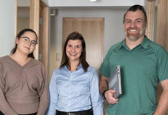 Three people are standing in a hallway.
