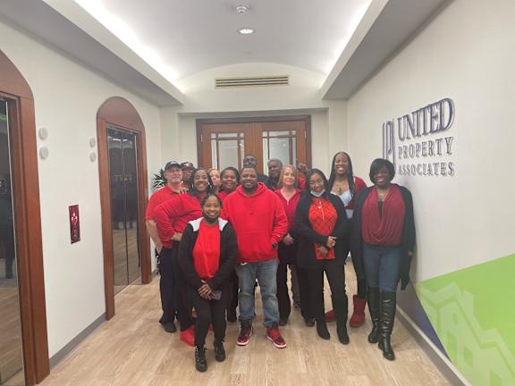 A group of people in red shirts are standing in a hallway with a United Property Associates logo on the wall.