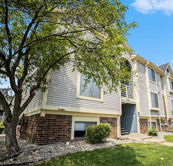 Exterior apartment building with a tree and bushes at Canal Club Apartments, Lansing