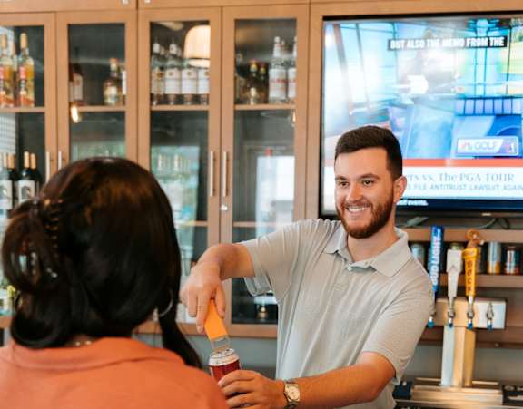 A man in a white shirt is standing behind a counter and serving a woman in an orange shirt.