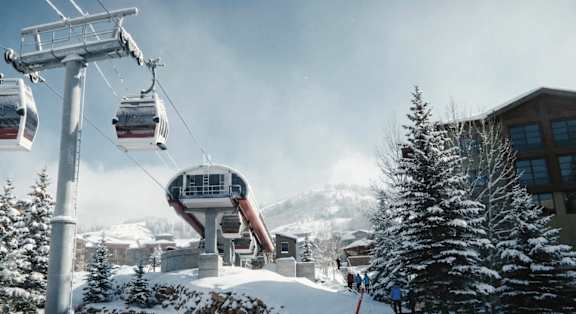 A ski lift with a chair lift car carrying people up a snowy mountain.