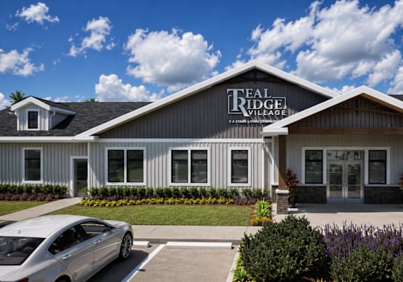 A silver car is parked in front of a building with a sign that says "TREAL RIDGE VILLAGE".
