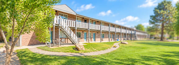 A building with a balcony and stairs is surrounded by green grass and trees.