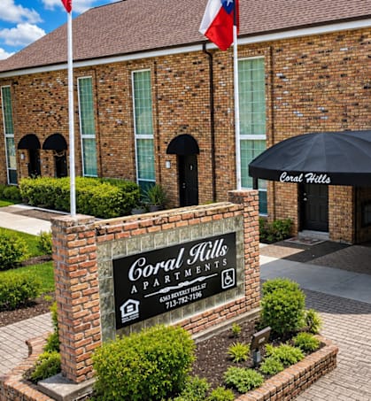 The front of a brick building with a sign that says "Coral Hills Apartment".