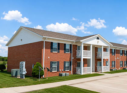 A red brick building with white trim and a parking lot in front.