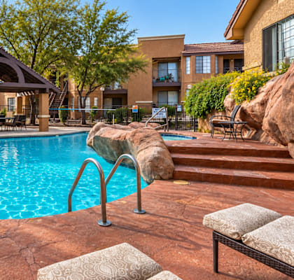A large outdoor swimming pool surrounded by a patio area with a rock and a bench.