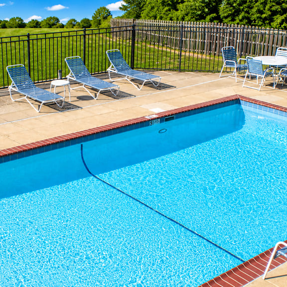 A pool surrounded by chairs and a fence.