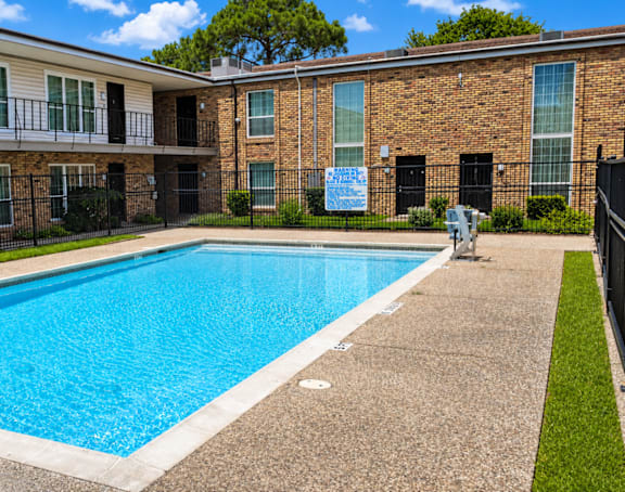 A swimming pool in front of a brick building with a sign that says "For Rent".