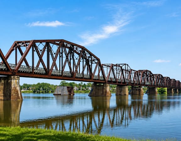 A large metal truss bridge spans over a calm body of water.