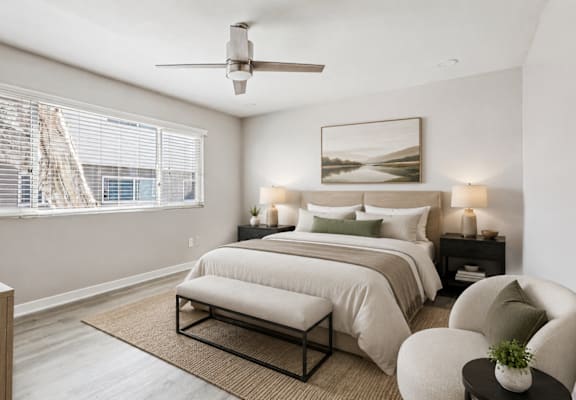 A bedroom with a large bed, a ceiling fan, and a window with blinds.