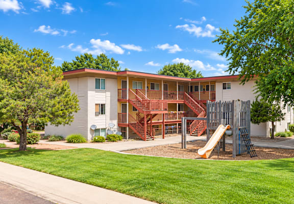 A playground with a slide is in front of a two-story building.