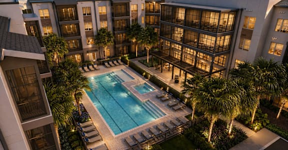 A swimming pool surrounded by palm trees and lounge chairs in front of a building.