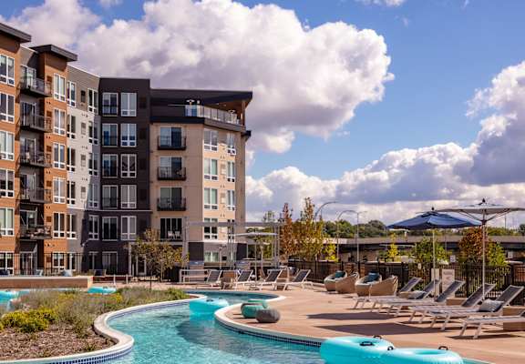 A large apartment complex with a pool and lounge chairs.