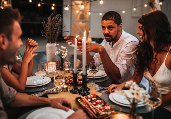A group of people are gathered around a dinner table with a lit candle and a cake on the table.