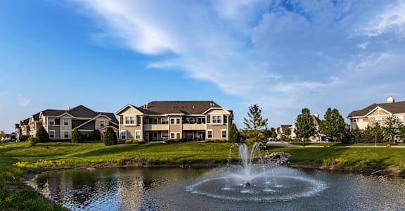 a fountain in the middle of a pond with houses in the background