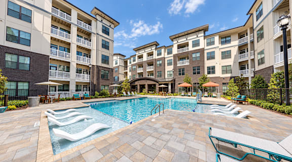 A large swimming pool surrounded by lounge chairs and apartment buildings.