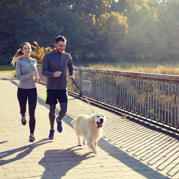 a man and a woman are running with a dog at The Exchange Apartments in New Brighton, Minnesota