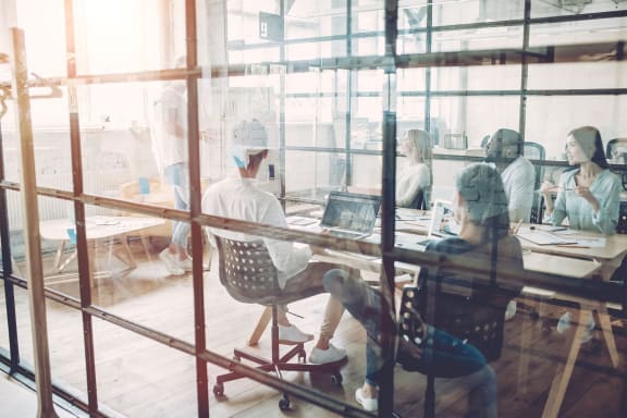 a group of people sitting at a table in an office with glass walls