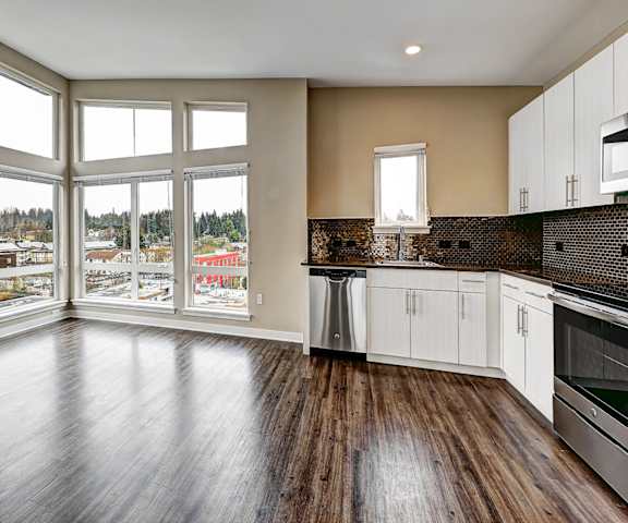 A large empty room with wooden floors and a view of a town through the windows.