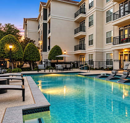 A large swimming pool in front of a building with lounge chairs around it.