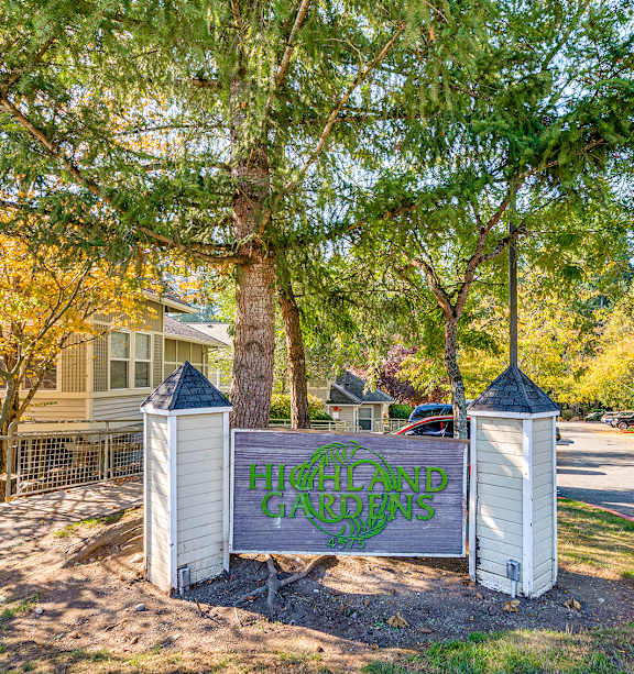 A sign that says "Hillcrest Gardens" is in front of a tree.