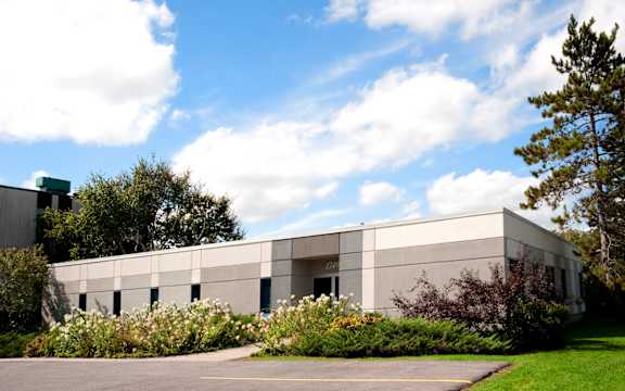 A modern building with a grey facade surrounded by greenery and a clear blue sky.