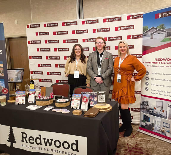 three people standing in front of a table with a table cloth and a sign that says red