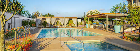 A pool surrounded by a concrete patio and a white fence.