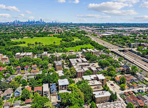 A cityscape with a mix of residential and commercial buildings, surrounded by greenery and a highway.