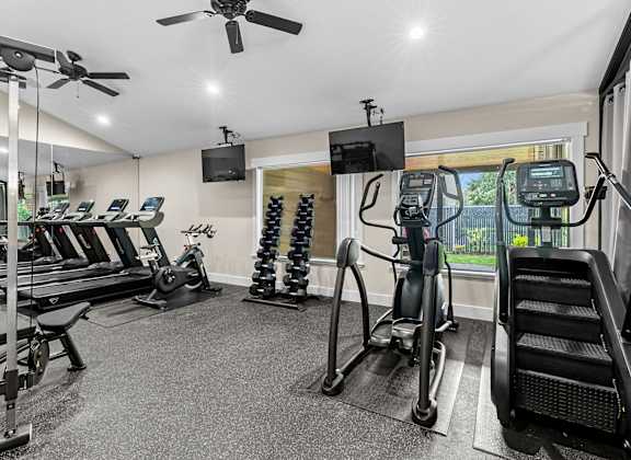 A spacious gym with treadmills, elliptical machines, and a fan.