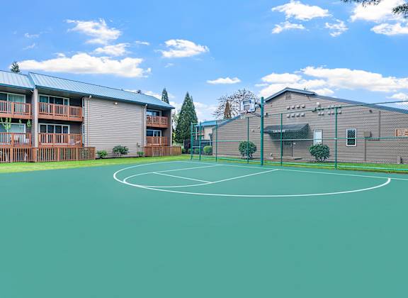 A basketball court is surrounded by a green fence and a building.