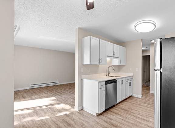 A kitchen with white cabinets and a black refrigerator and a view of the living room