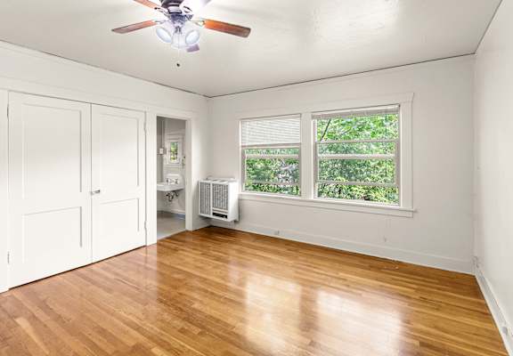 A room with a ceiling fan and a window with a view of trees.